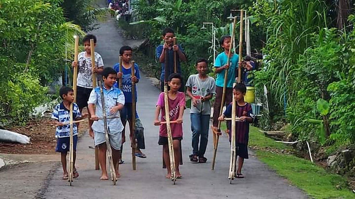 Anak-anak bermain egrang menyusuri jalan Padukuhan Sinom